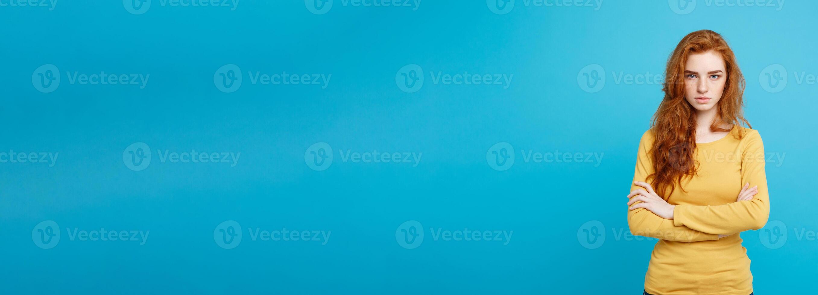 Portrait of young beautiful ginger woman with tender serious face crossing arms looking at camera. Isolated on pastel blue background. Copy space photo