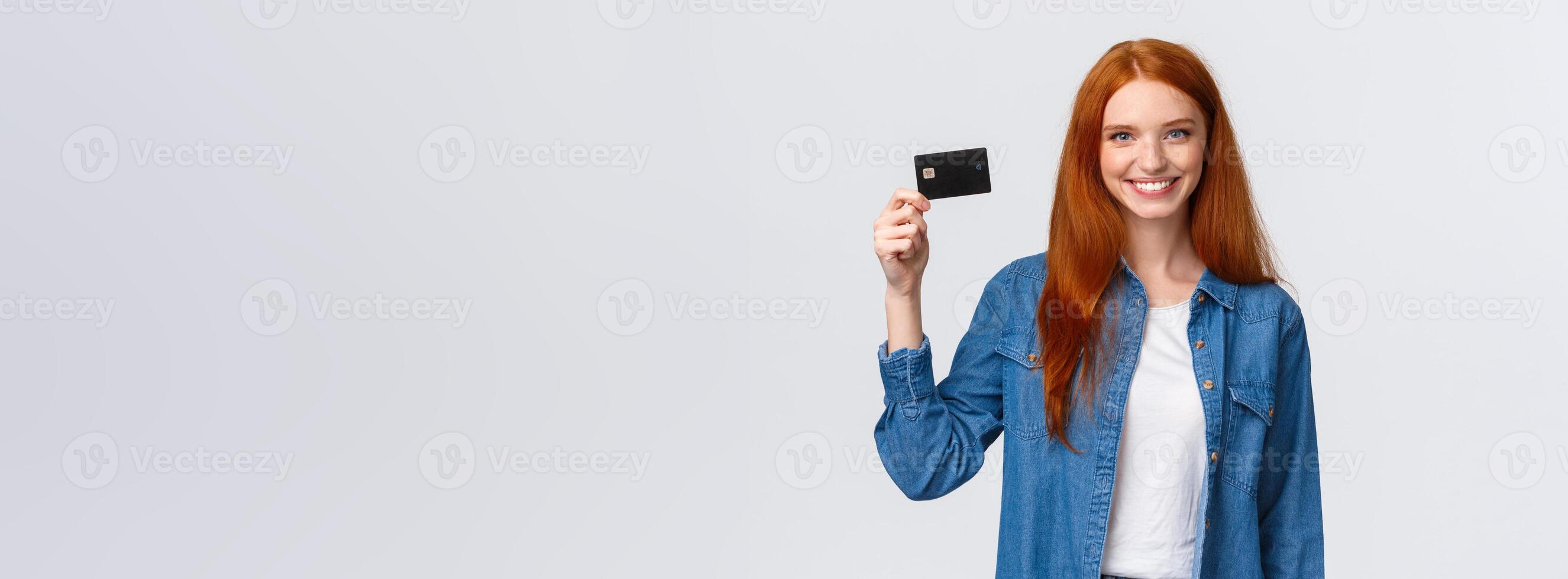 Bank, finance and education concept. Cheerful redhead girl working part-time, receive her first paycheck, holding credit card and smiling confident, standing white background delighted photo