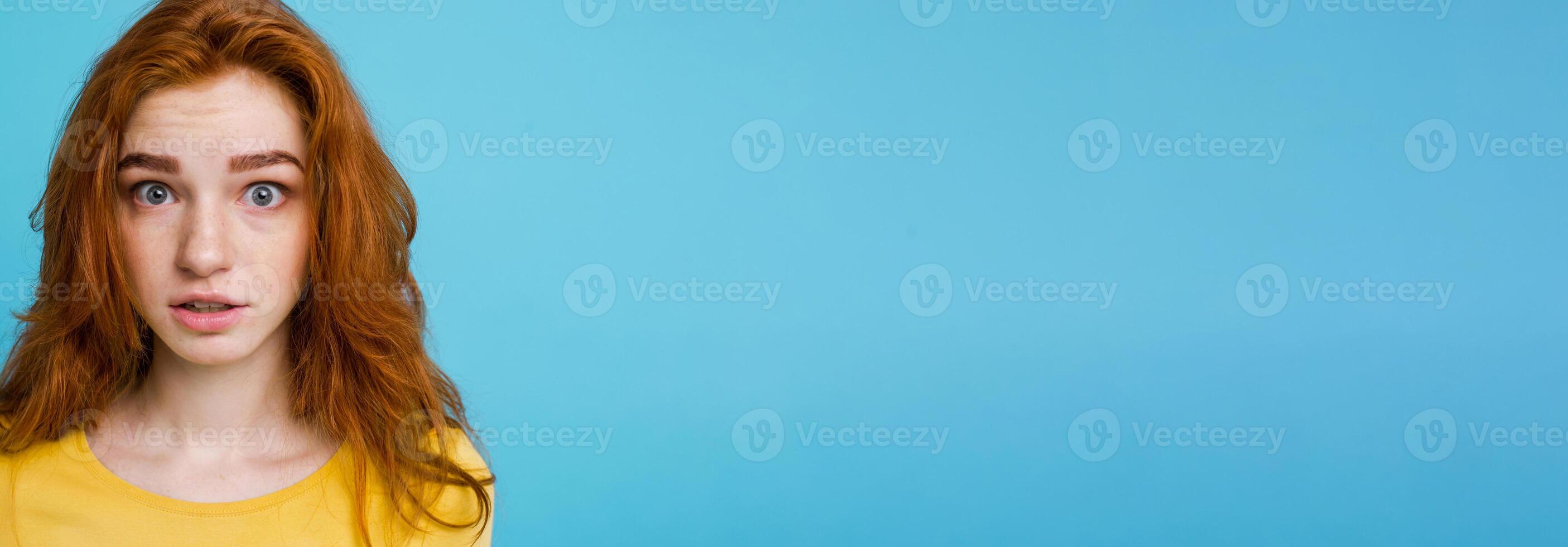 Headshot Portrait of happy ginger red hair girl with freckles smiling looking at camera. Pastel blue background. Copy Space photo