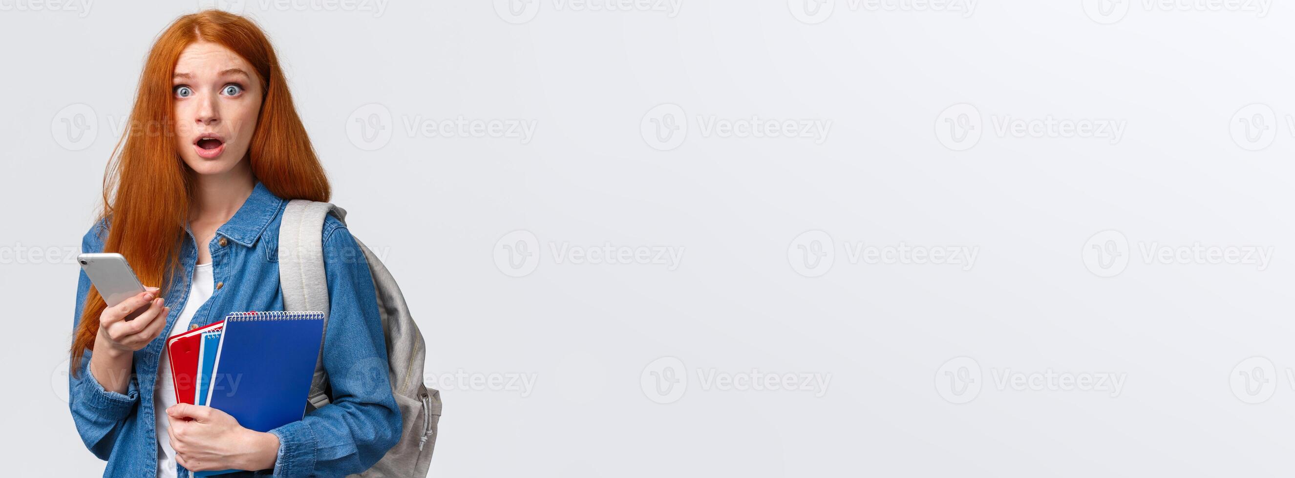 Freshman girl with red long hair, dont know where her class, looking questioned and confused, stare worried, holding smartphone, backpack and notebooks, clueless where go, white background photo