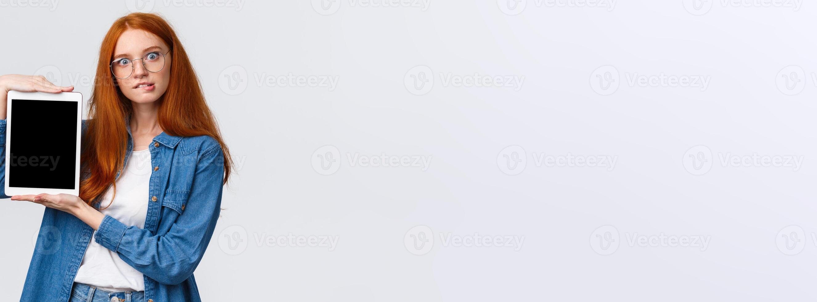 Cant resist temptation, add to cart now. Tempting and curious good-looking excited redhead woman in glasses, biting lip desire buy something online, showing digital tablet screen, white background photo