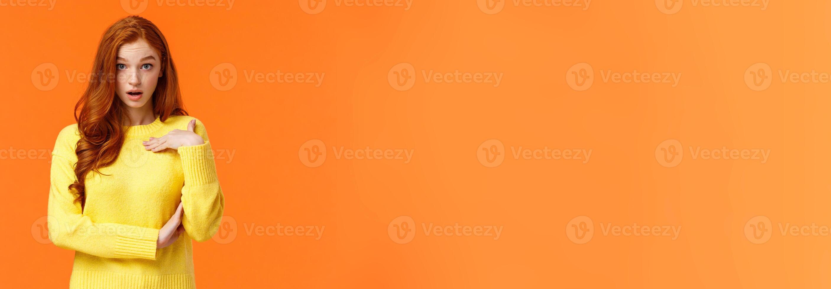 Who me. Frustrated and shocked, confused redhead woman accused, pointing herself and gasping stare astounded, feeling hurt person blame her, receive accusations, orange background photo