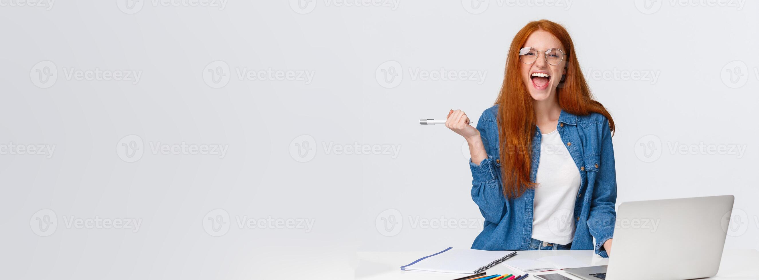 Excited and triumphing good-looking redhead female student passed challenge, found out final exam rating online using laptop, holding pen and screaming happily, standing white background photo