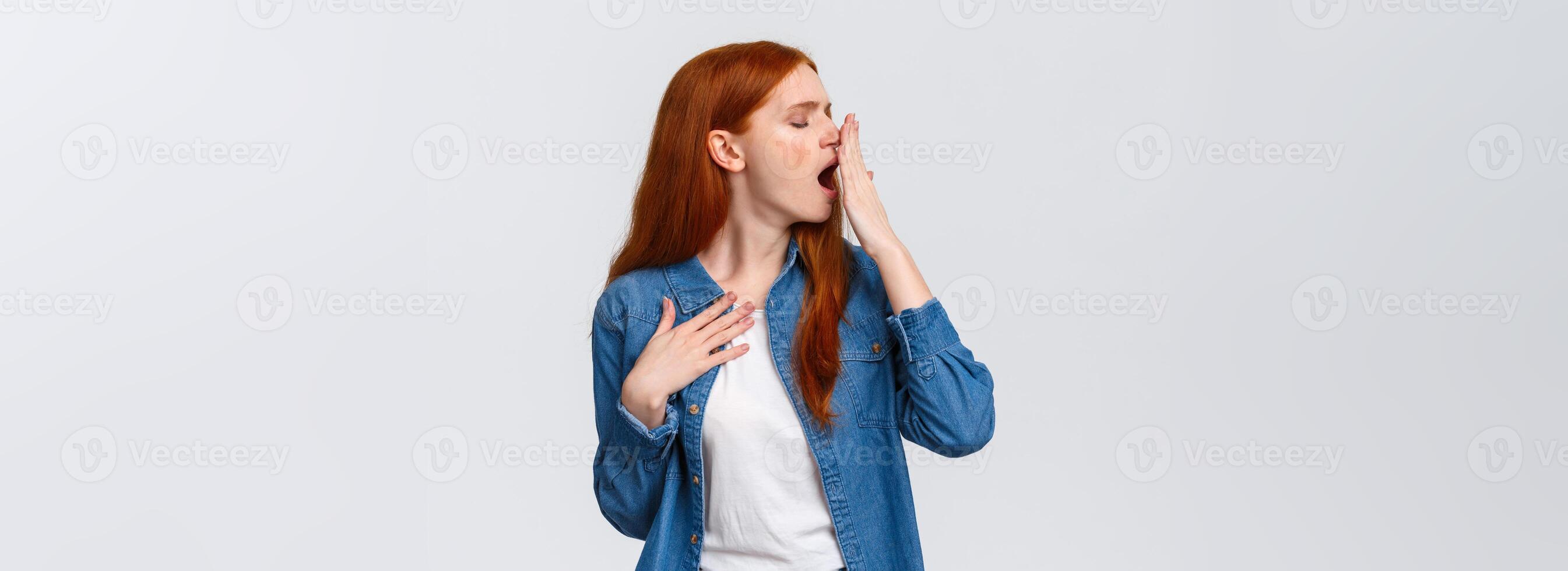 Waist-up portrait lovely redhead girl want sleep, feeling tired or bored, turn head away and yawn, cover opened mouth with palm, yawning over white background after boring class, white background photo