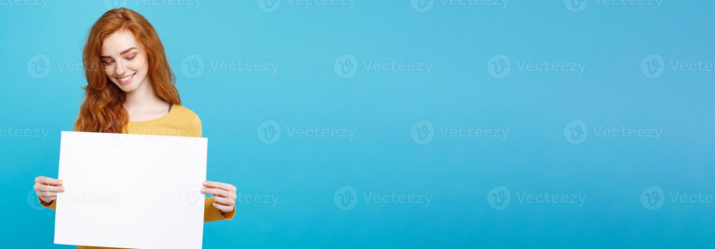 Close up Portrait young beautiful attractive ginger red hair girl smiling showing blank sign. Blue Pastel Background. Copy space. photo