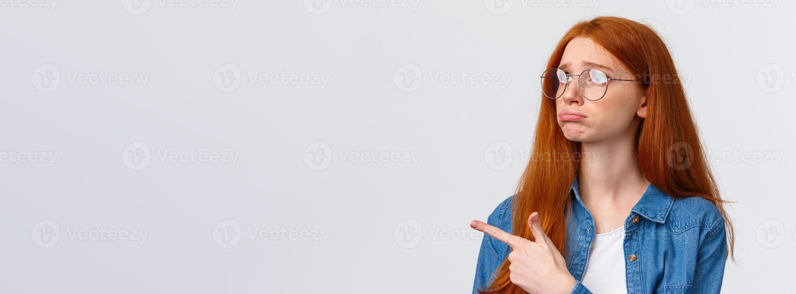 Close-up portrait gloomy and sad pouting cute redhead girl with lovely blue eyes, wear glasses, sulking and sobbing sad, pointing looking upper left corner with regret or jealousy, want something photo