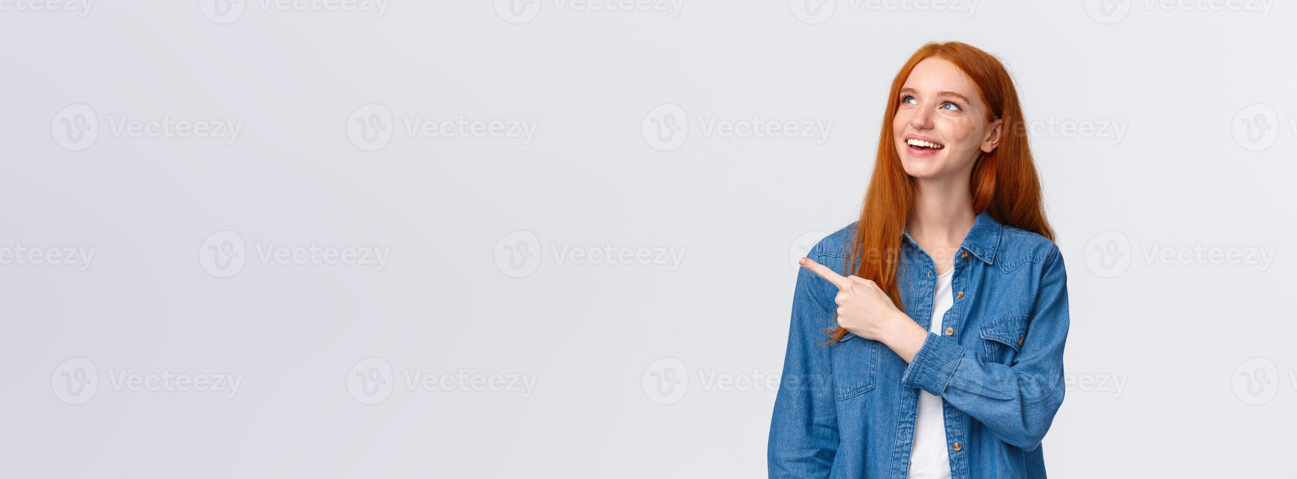Dreamy carefree good-looking redhead european woman in denim shirt, looking pointing upper left corner, smiling delighted, making choice, seeing perfect product, recommend company service photo