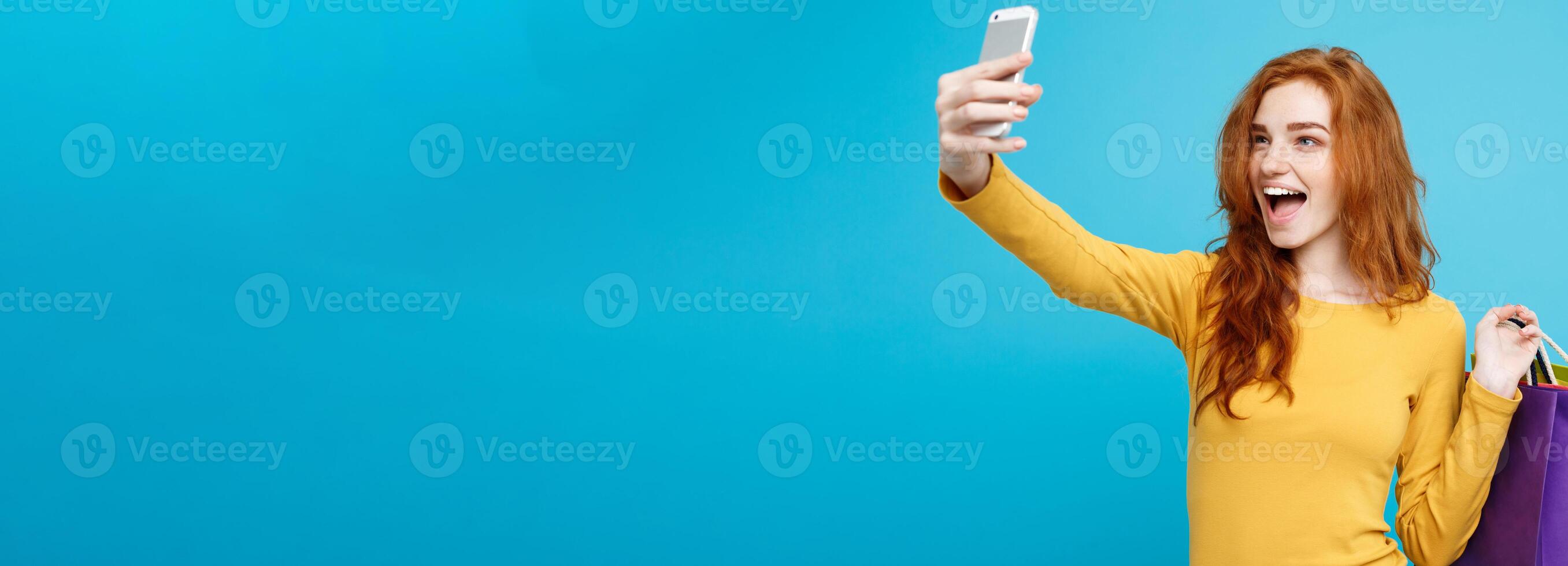 Shopping Concept - Close up Portrait young beautiful attractive redhair girl smiling looking at camera with white shopping bag and selfie. Blue Pastel Background. Copy space photo
