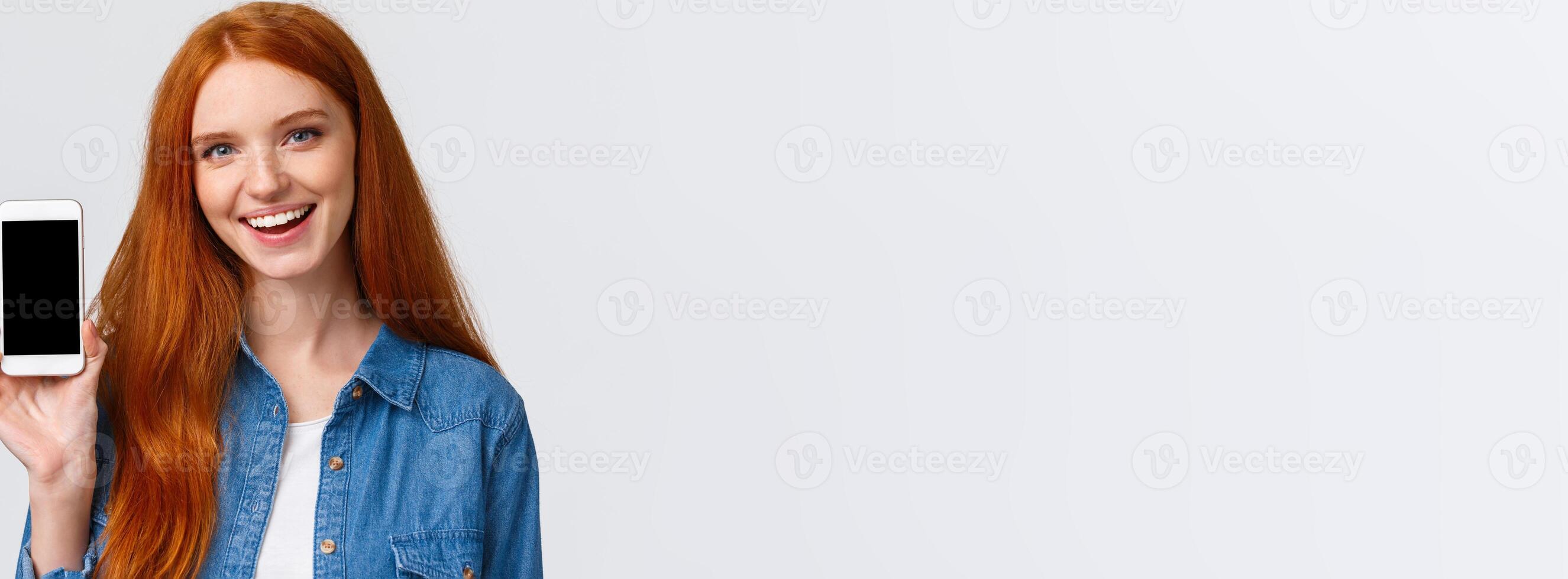 Close-up portrait modern millennial cute redhead female with blue eyes, advice get cool new app, showing smartphone display and smiling, advertising game or photo filter application