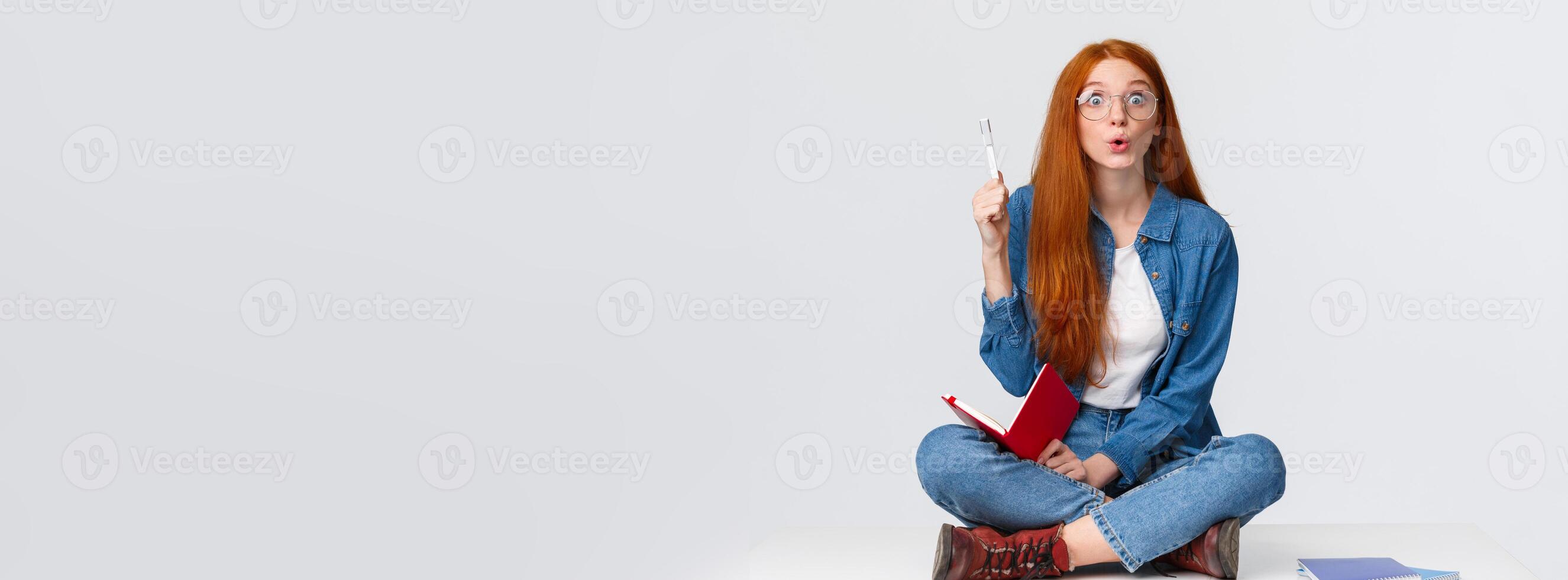 Talented and smart cute redhead teenage student, college girl solving exercise for homework, got solution, thinking of plan, sitting on floor with notebook, raising pen up eureka, saying her thought photo