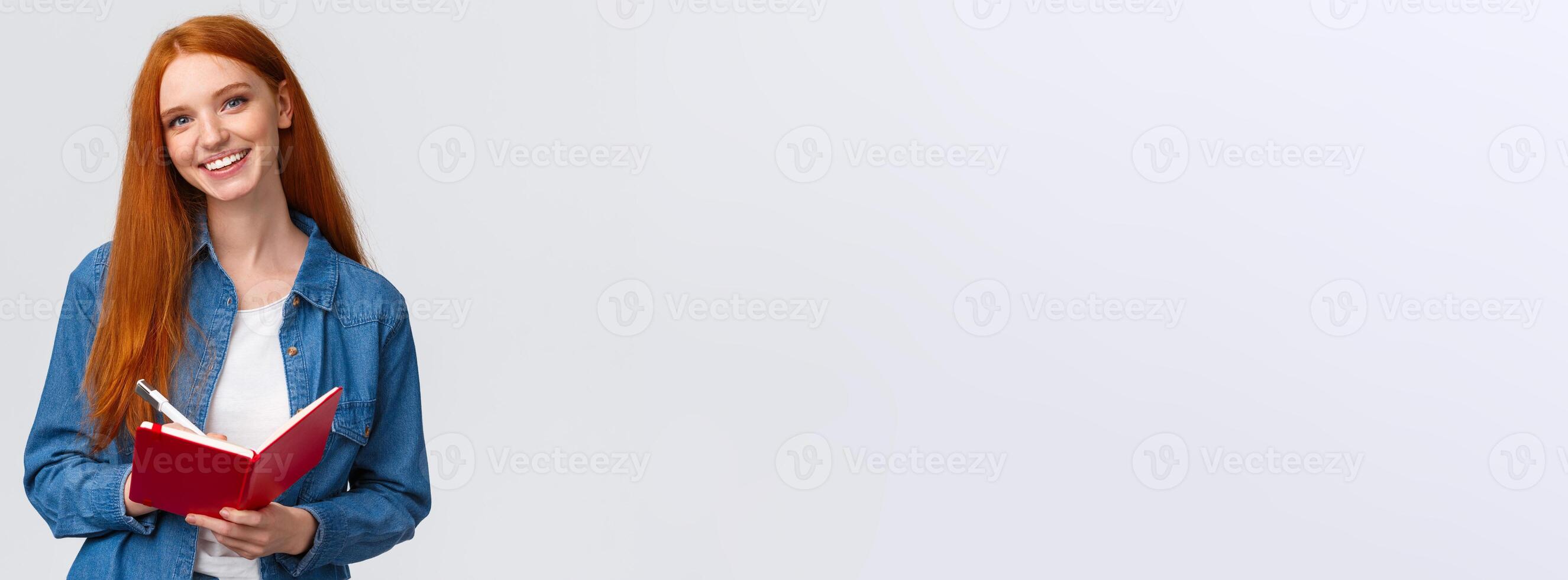 Charismatic talented cute redhead female student studying, taking notes after teacher in notebook, writing in diary, drawing doodles standing white background cheerful photo