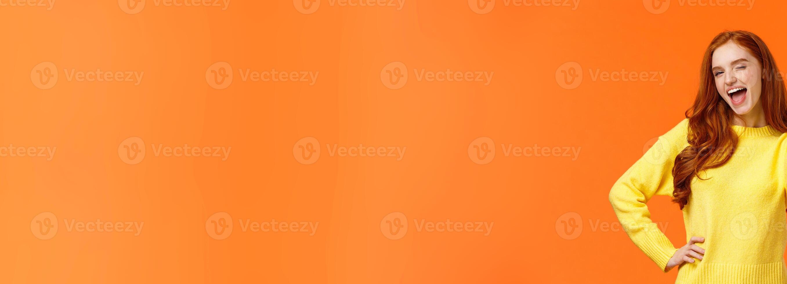 Saying yes. Cheerful redhead woman in yellow sweater giving thumb-up gesture and wink, encouraging keep-up, approving idea, express positive opinion, recommend product or event, orange background photo