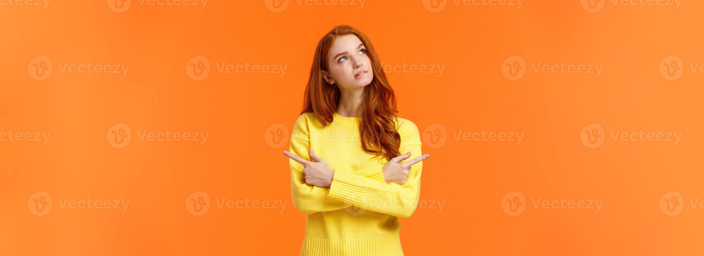Pensive girl trying make decision, thinking, looking upper left corner thoughtful, pondering what buy for holidays, pointing sideways left and right, looking up dreamy, orange background photo