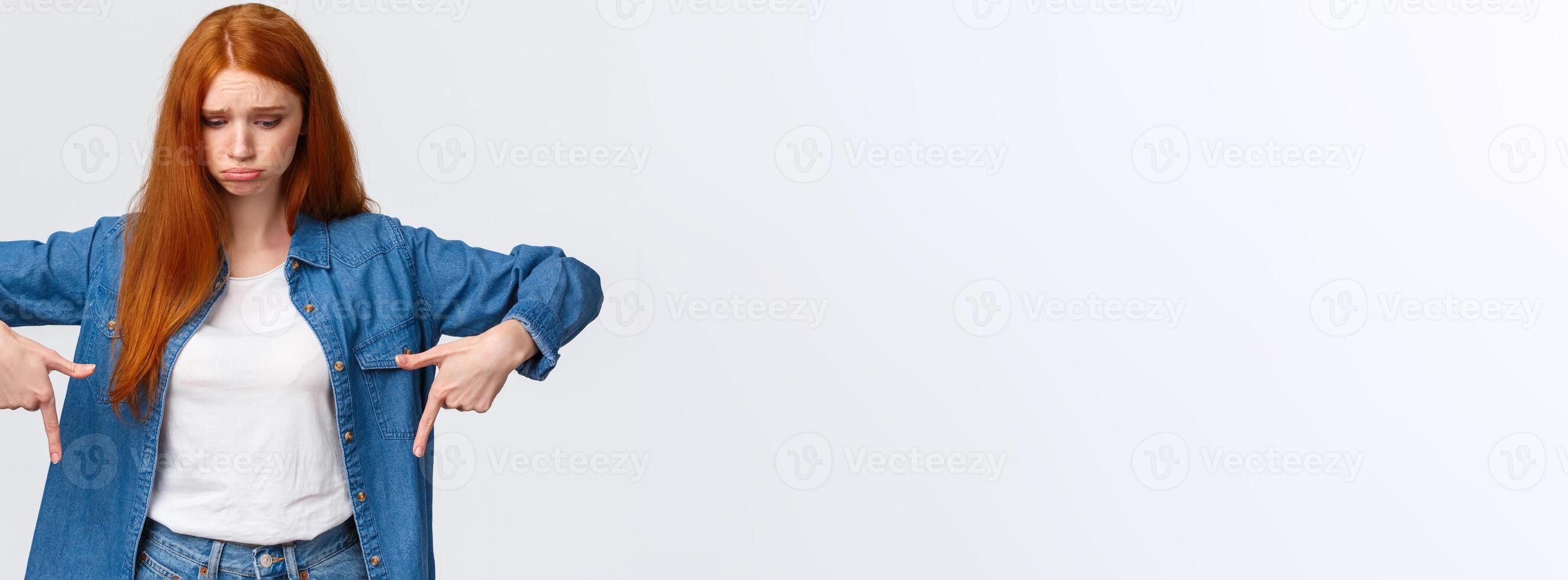Upset, gloomy timid redhead teenage girl express pity or jealousy, regret something broken, sobbing, pouting sad and looking pointing down distressed, standing unhappy over white background photo