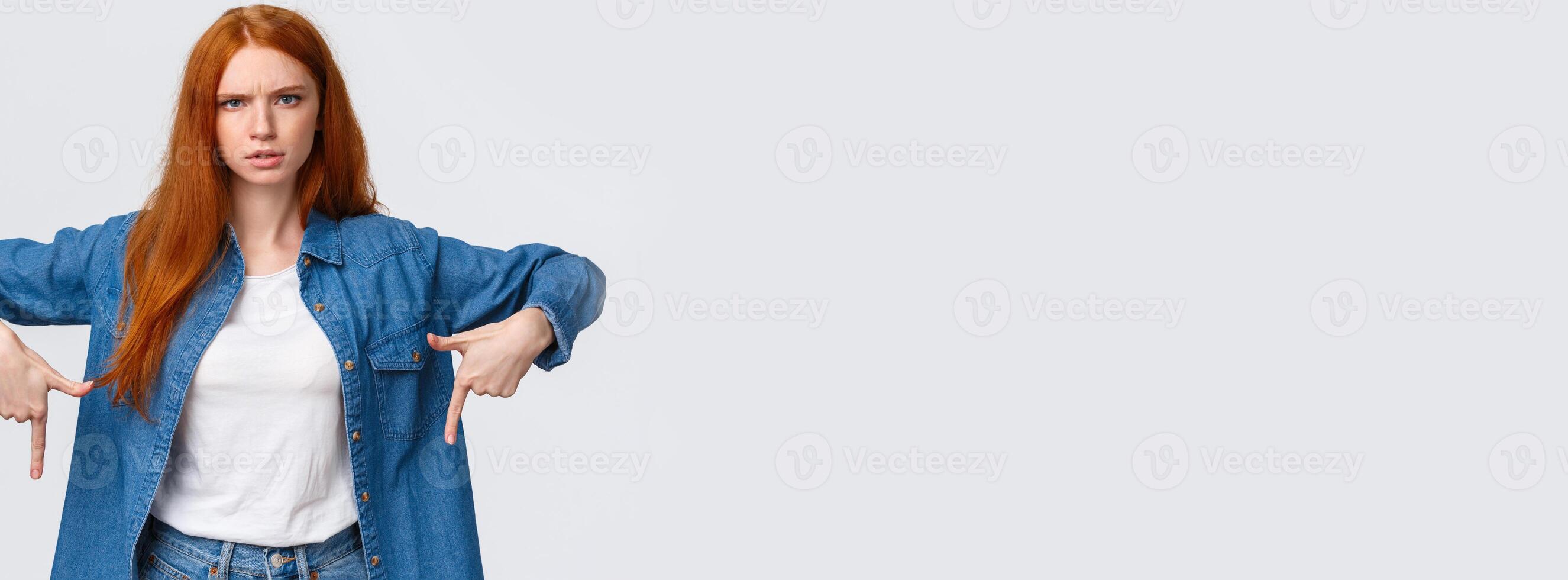 Mad and disturbed, questioned redhead woman waiting answer on question, pointing fingers down, frowning angry and distressed, cat made mess while she was at work, scolding over white background photo