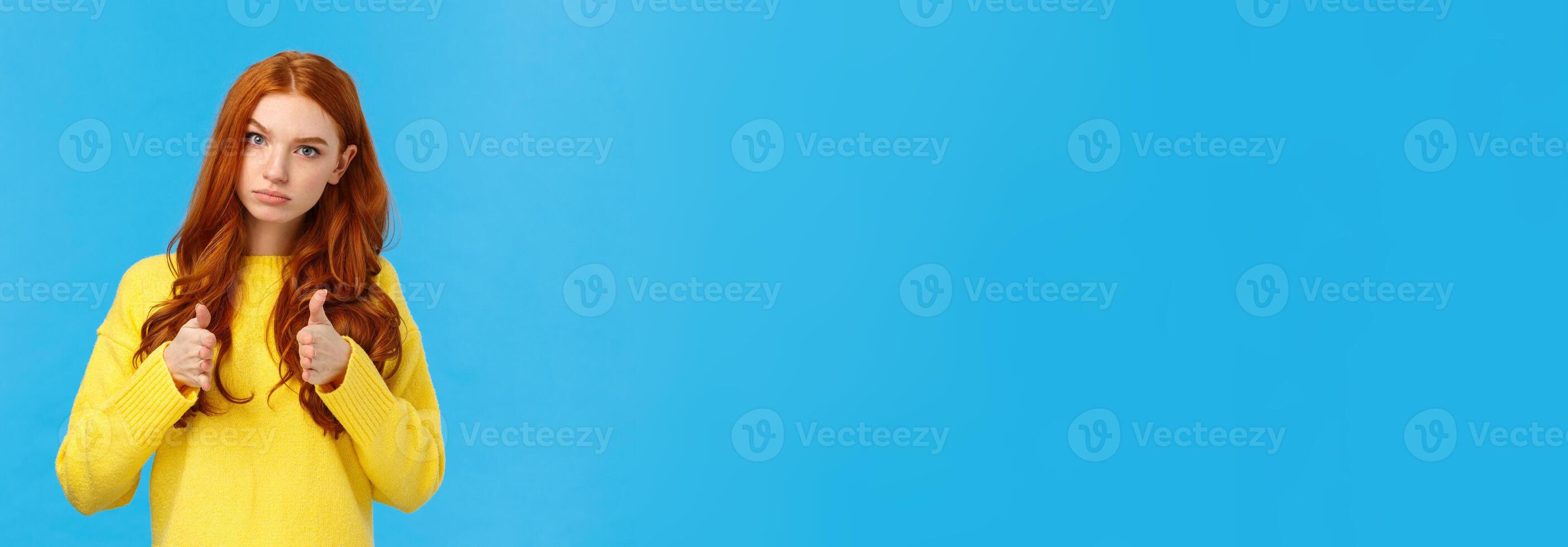 Serious and determined supportive redhead girlfriend, showing you can do it, encourage friend, make thumbs-up in approval, rooting for you, glance with confident expression, blue background photo