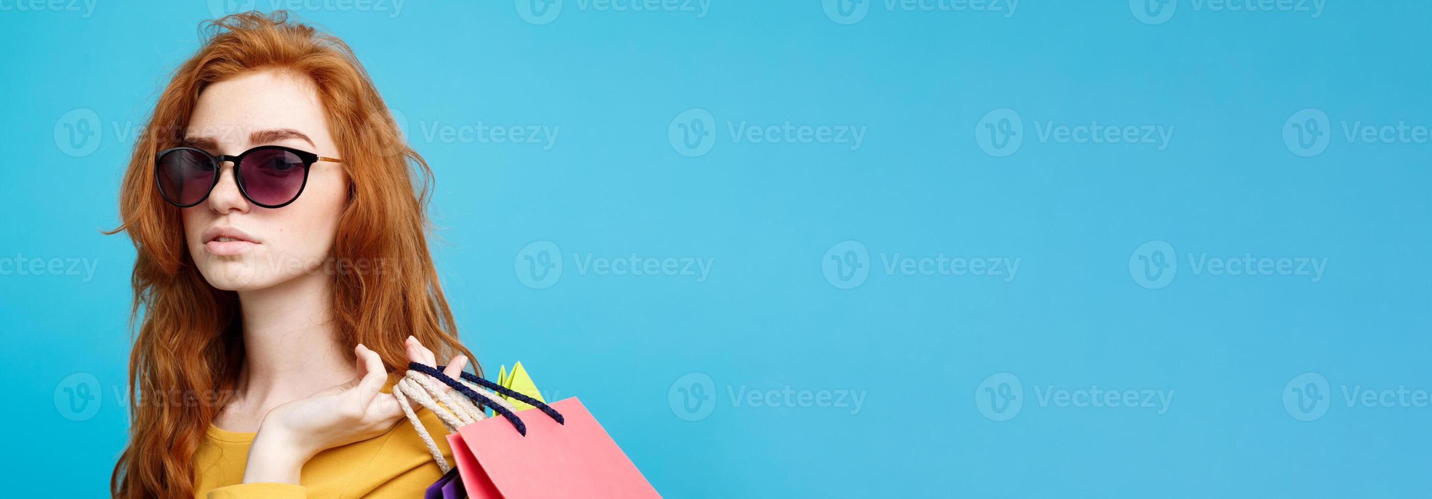 Shopping Concept - Close up Portrait young beautiful attractive redhair girl smiling looking at camera with shopping bag. Blue Pastel Background. Copy space. photo
