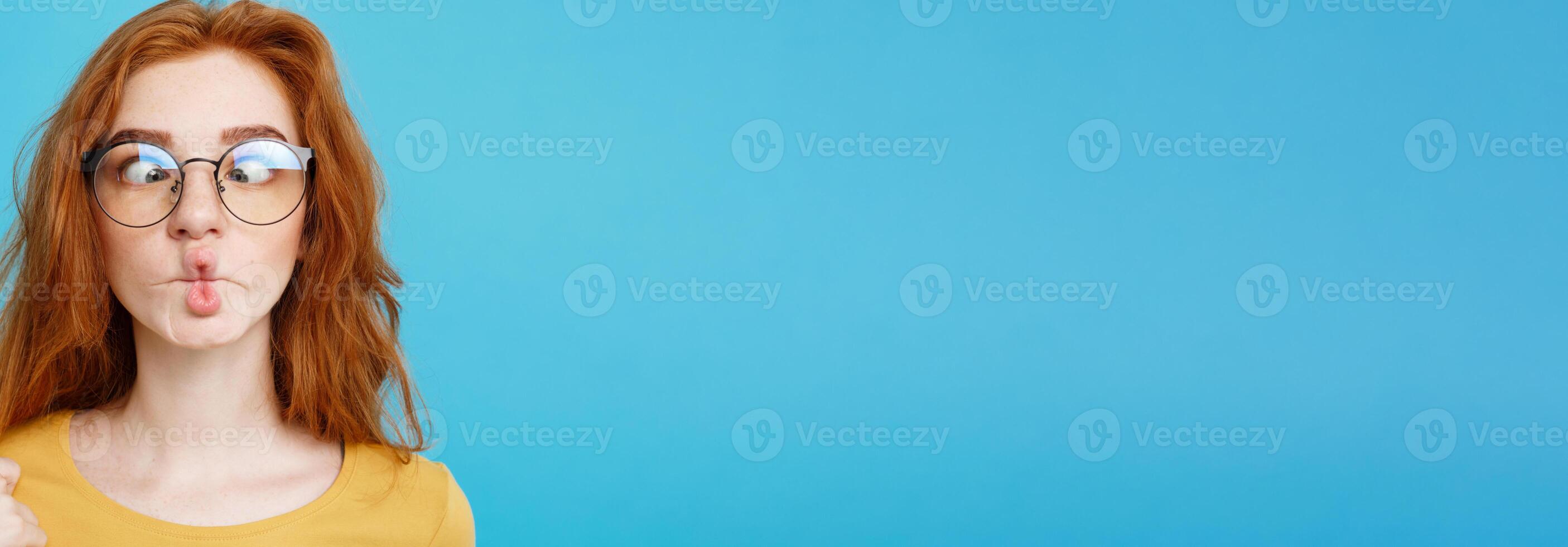 Headshot Portrait of happy ginger red hair girl with freckles smiling looking at camera. Pastel blue background. Copy Space. photo