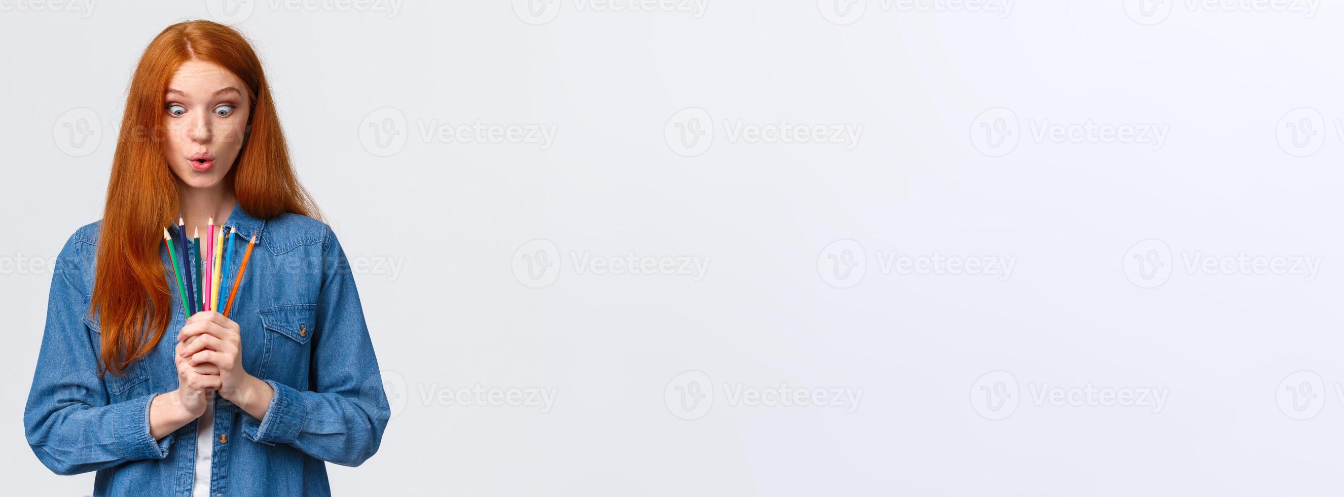 Girl eager start new art course, learn how to design, make models, standing with colored pencils, folding lips amused, looking at tools wondered and thrilled, drawing over white background photo