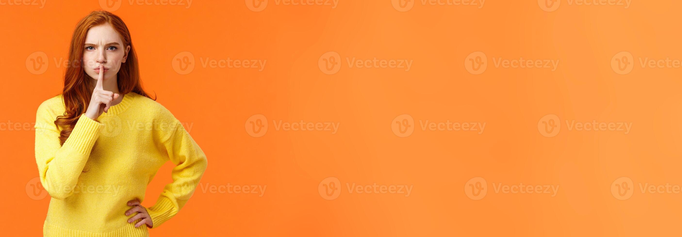Serious and mad elder sister say keep silent, forbid talking during class, shushing angry with index finger pressed mouth, hold hand on waist in dissatisfied pose, standing orange background photo