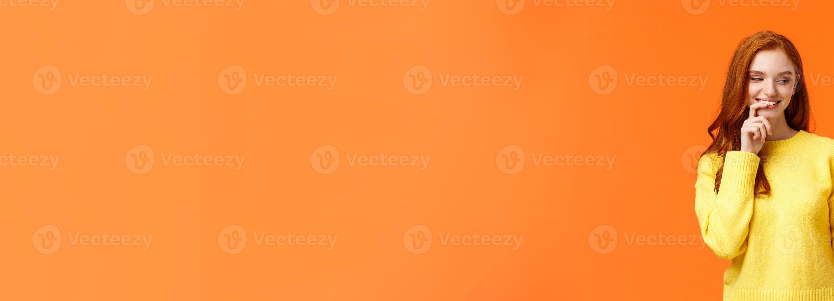 Cheerful and satisfied, happy redhead woman have cheat-day eating delicious food, holding tasty piece cake, biting lip and smiling, cant resist temptation, desire take bite, orange background photo