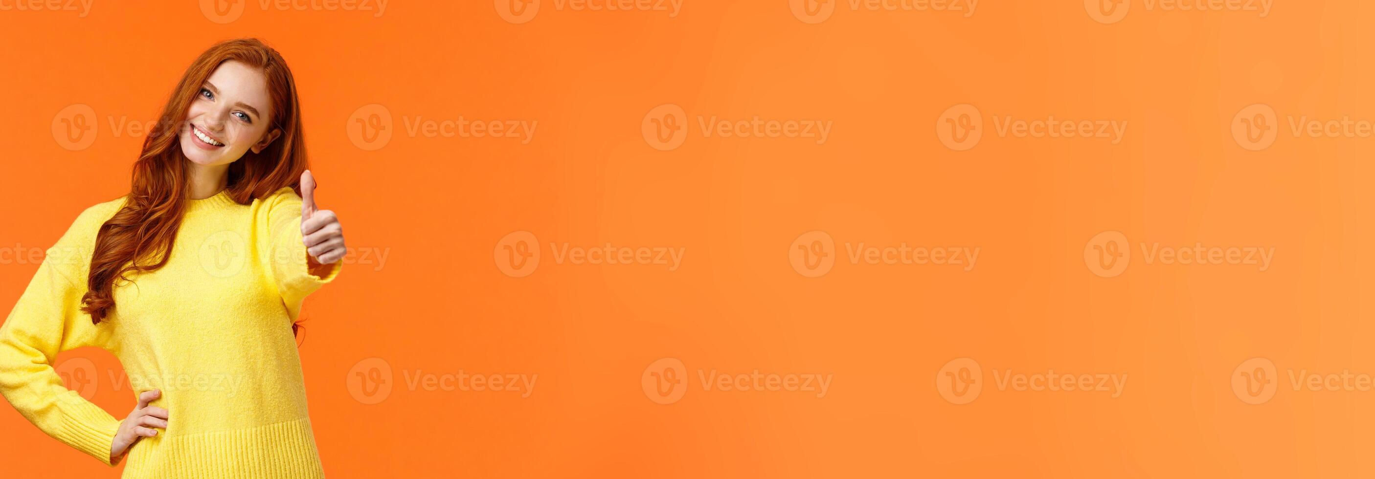 Girl giving permission, say yes. Cheerful redhead woman in yellow sweater extend arm and show thumb-up, smiling nod agreement, give approval, like idea, standing orange background joyful photo