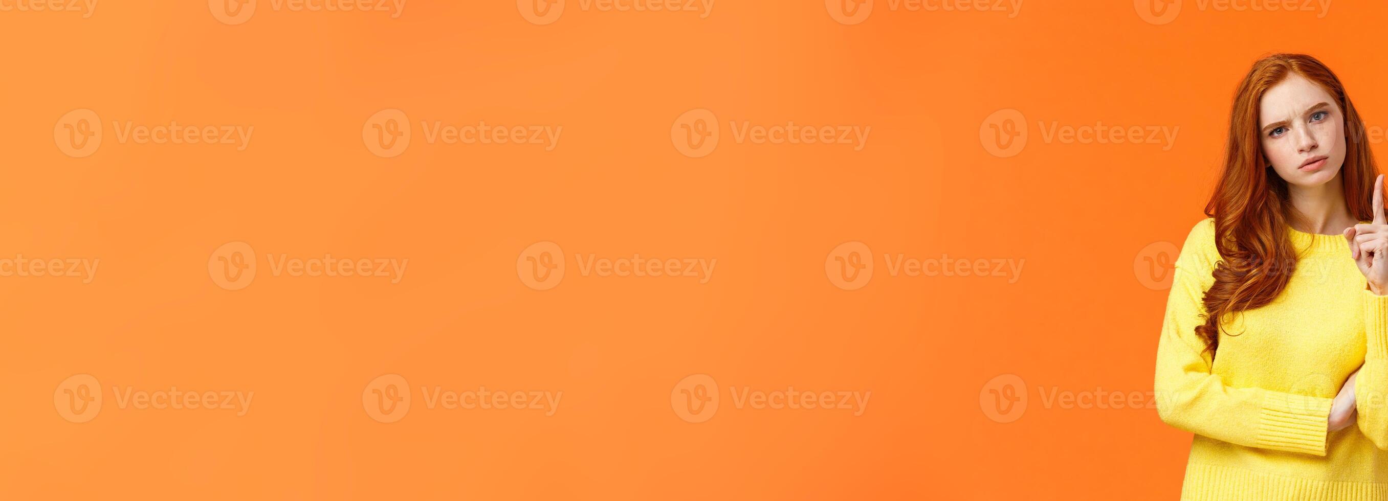 Redhead girl express disapproval as shaking her finger at someone with disappointed angry face, frowning give warning, prohibit unacceptable behaviour, standing displeased orange background photo