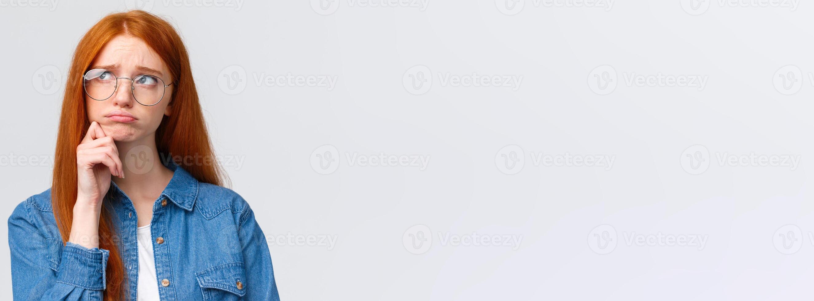 Uneasy sulky cute timid redhead college girl in glasses, look up thoughtful and dreamy, pouting unhappy feeling sad, regret comming party, standing white background indecisive and upset photo