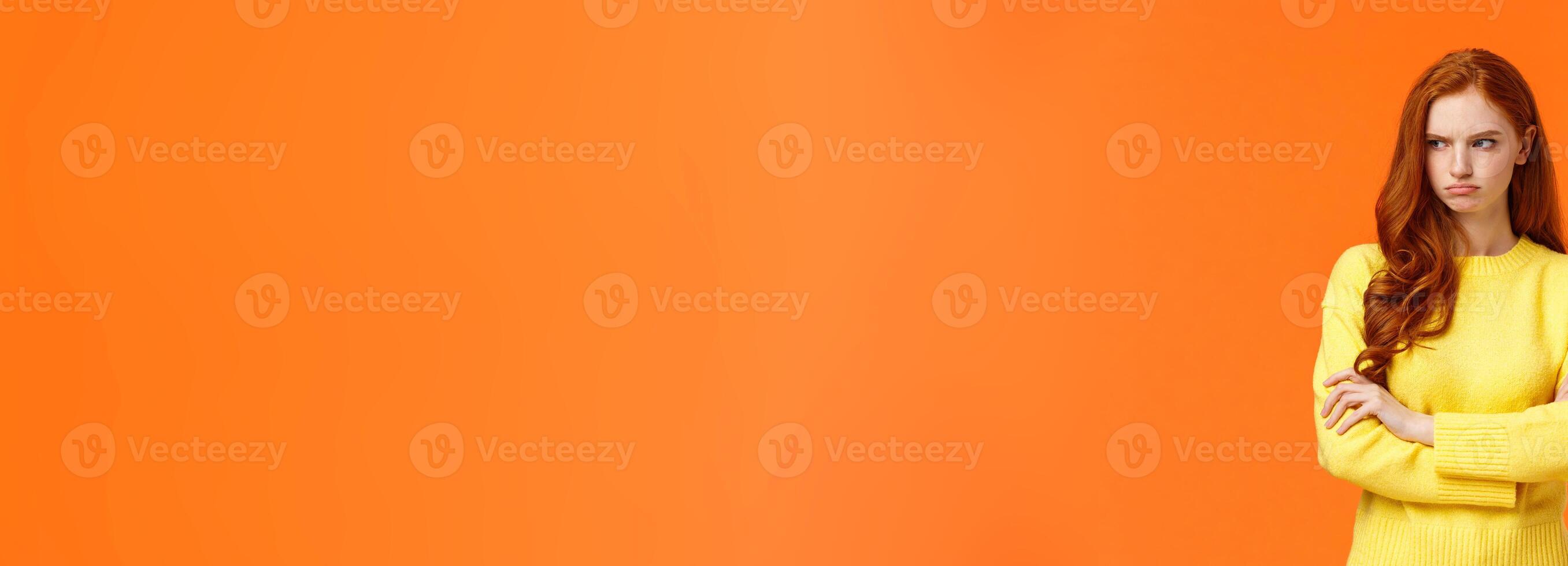 Offended angry and tensed woman with curly red hair, freckles, having bad mood, cross arms chest, thinking troublesome situation, frowning getting mad, standing orange background distressed photo