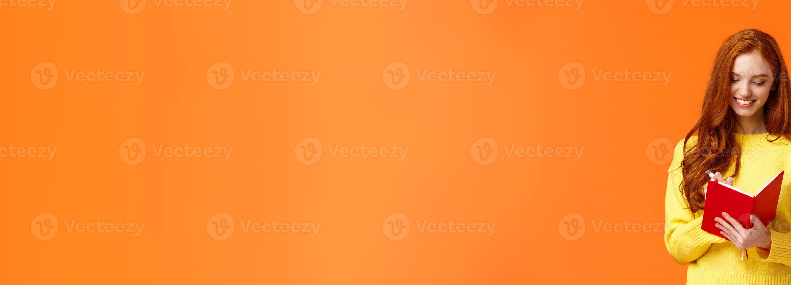 Waist-up portrait attractive redhead girl 20s write in her diary, fill-in to-do list or personal schedule in new notebook, smiling as having everything planned, standing orange background carefree photo