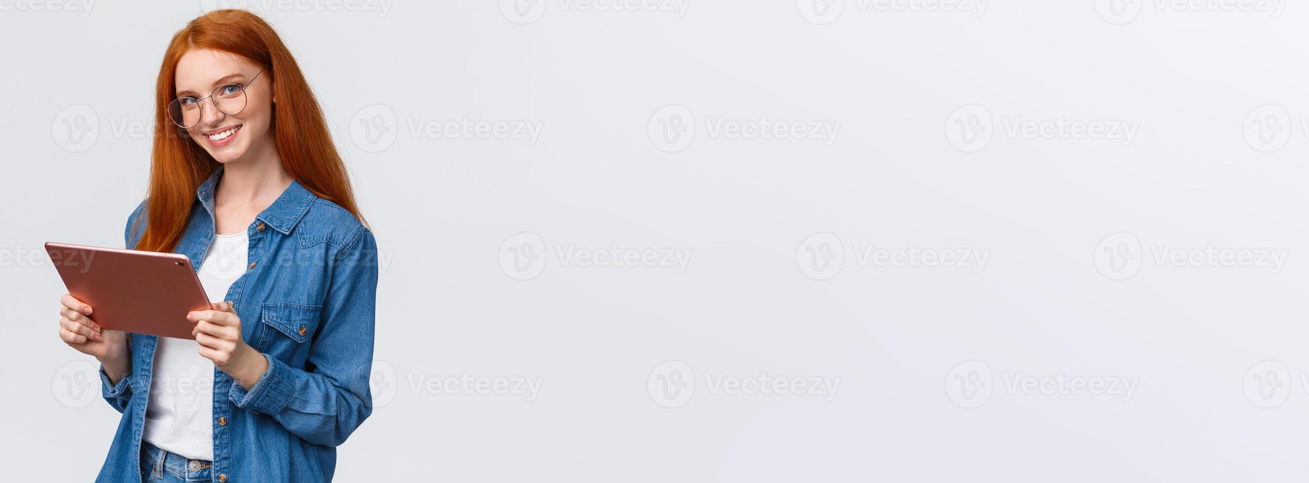 Professionalism, work and people concept. Young cheerful attractive female redhead in glasses, holding digital tablet and smiling at camera with happy confident expression over white background photo