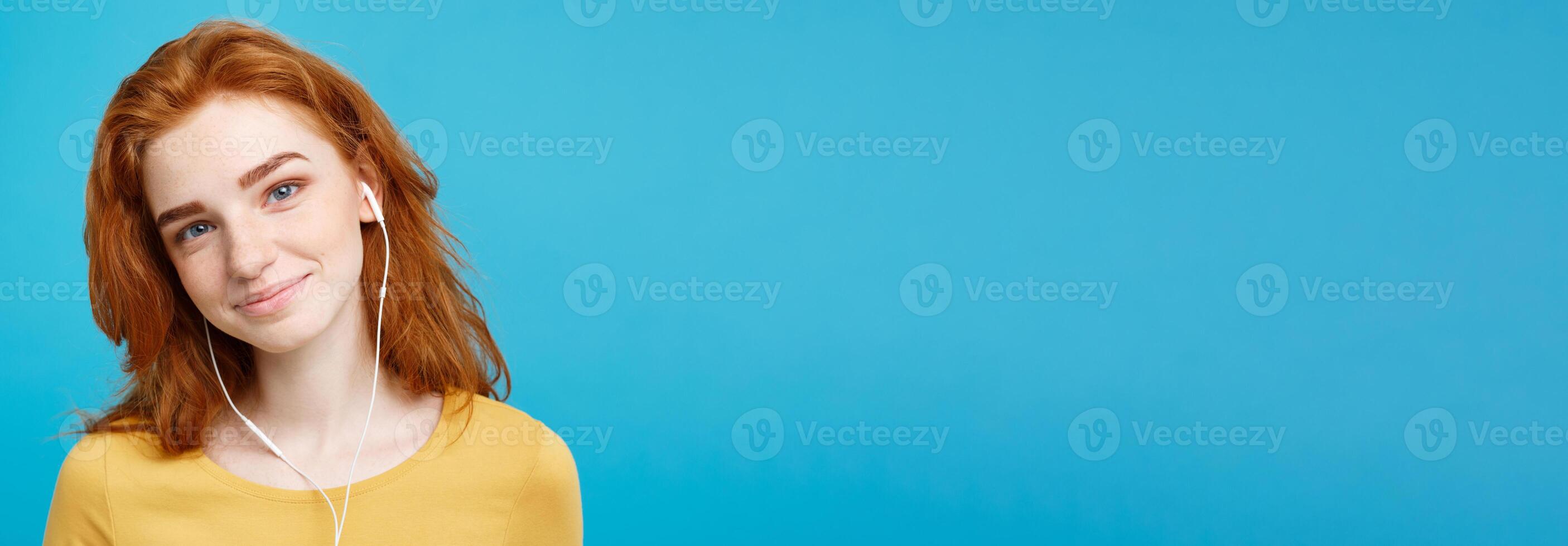 Lifestyle concept - Portrait of cheerful happy ginger red hair girl enjoy listening to music with headphones joyful smiling to camera. Isolated on Blue Pastel Background. Copy space. photo