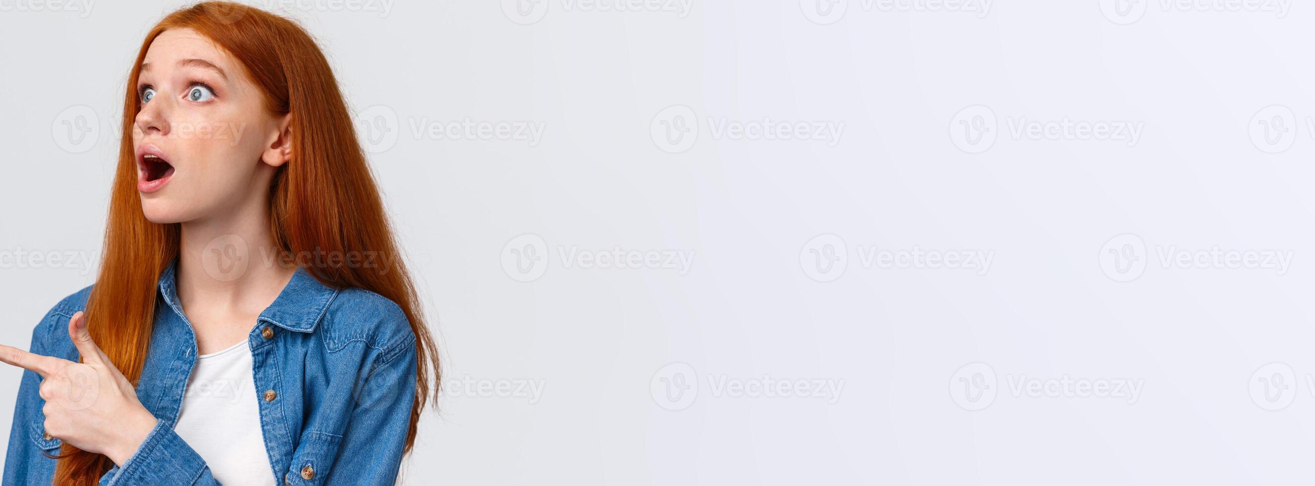 Have you seen it. Close-up astonished and impressed shook redhead girl saw something impressive, open mouth excited, pointing finger left, watching awesome performance, white background photo