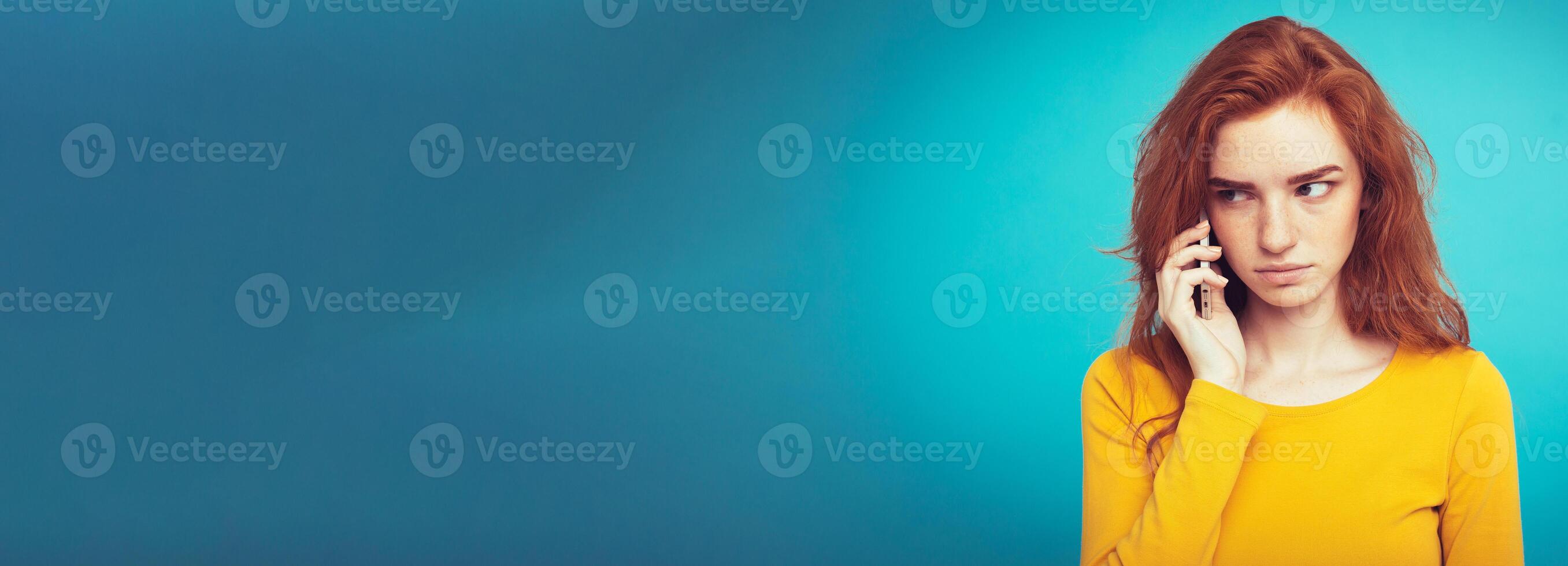 Lifestyle concept - Portrait of ginger red hair girl with shocking and stressful expression while talking with friend by mobile phone. Isolated on Blue Pastel Background. Copy space photo