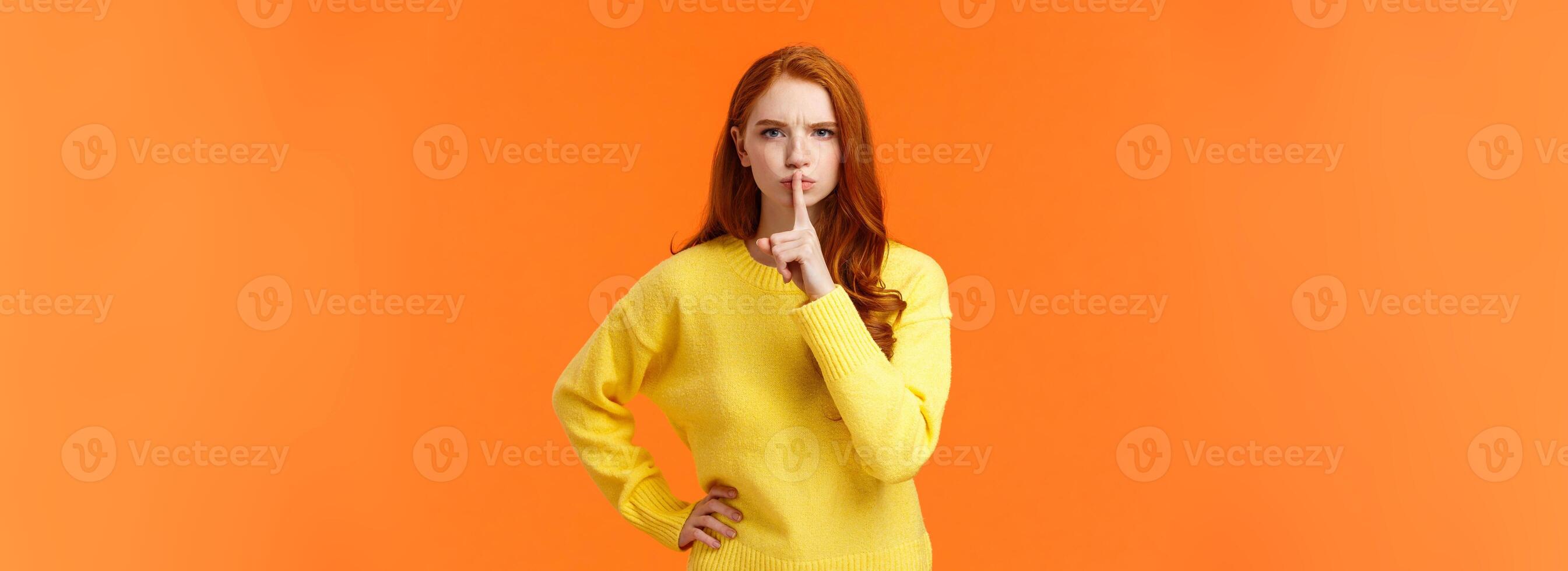 Serious and mad elder sister say keep silent, forbid talking during class, shushing angry with index finger pressed mouth, hold hand on waist in dissatisfied pose, standing orange background photo