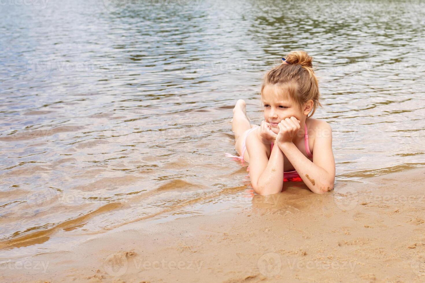 close-up portrait happy girls on the beach during summer holidays. girl lies on the beach and joyfully looks at the water photo