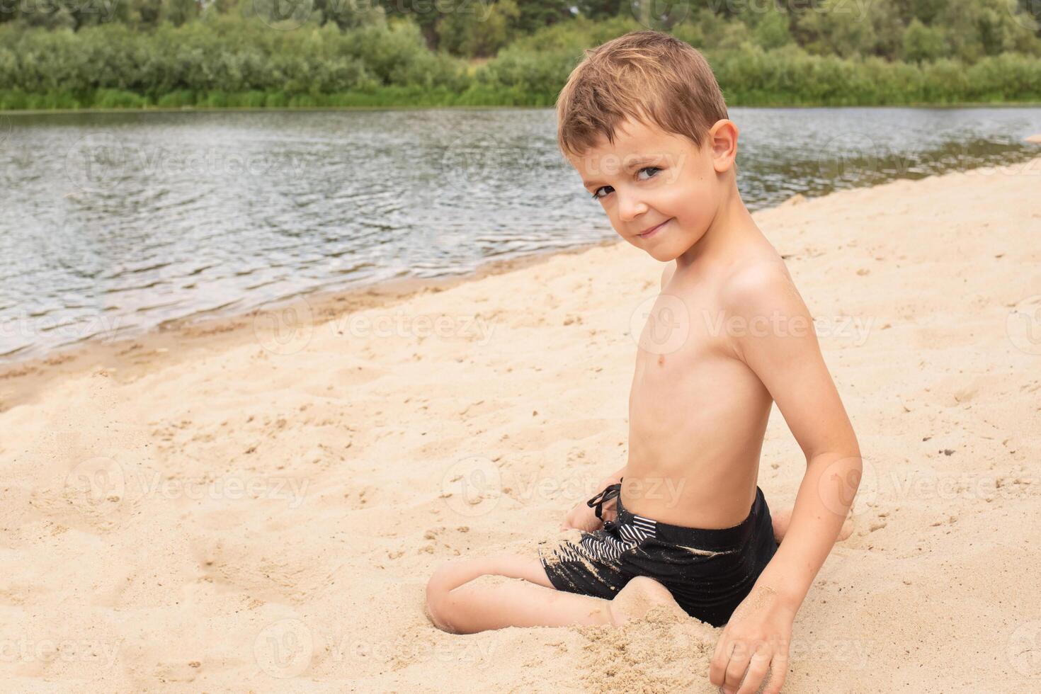 close-up portrait happy boy on the beach during summer vacation. children play on a lake surrounded by green forest on weekends. background photo