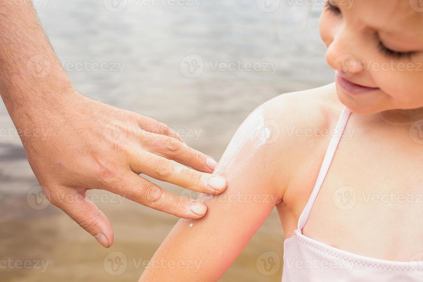close-up portrait happy girls on the beach during summer holidays. parent applies sunscreen to child. children play on a lake surrounded by green forest on weekends photo