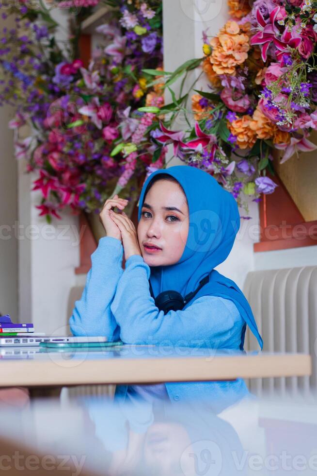 portrait of beautiful adult asian woman wearing elegant headscarf with hands parallel to the side of her cheek in indoor coffee shop. for advertising content, lifestyle, technology photo