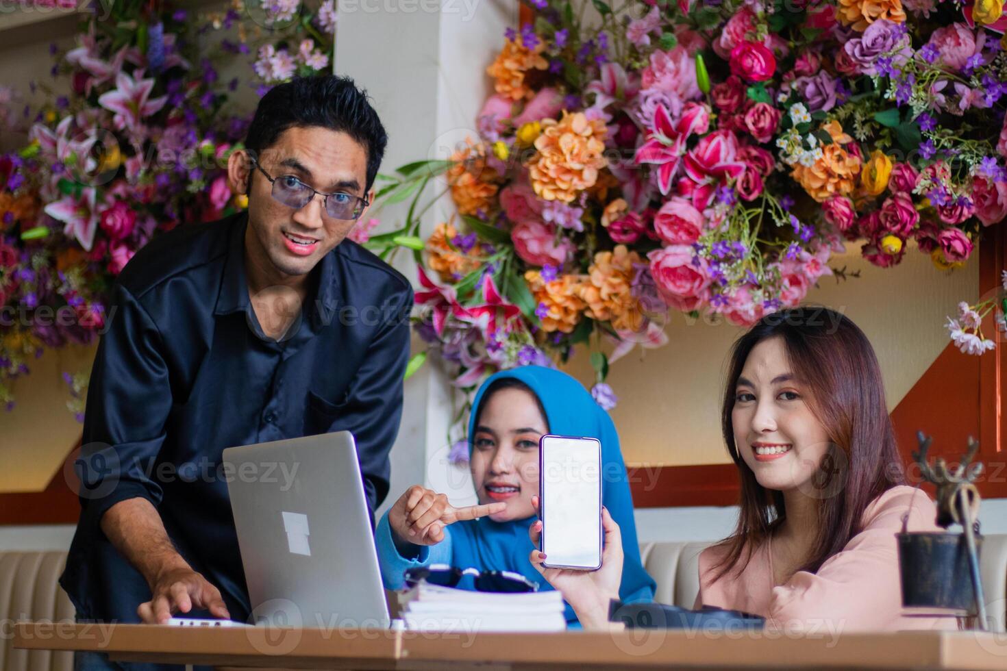 Group of cheerful Asian workers showing mobile phone screen in front of laptop computer from government in coffee shop cafe. for group, company, education, education, business concept photo
