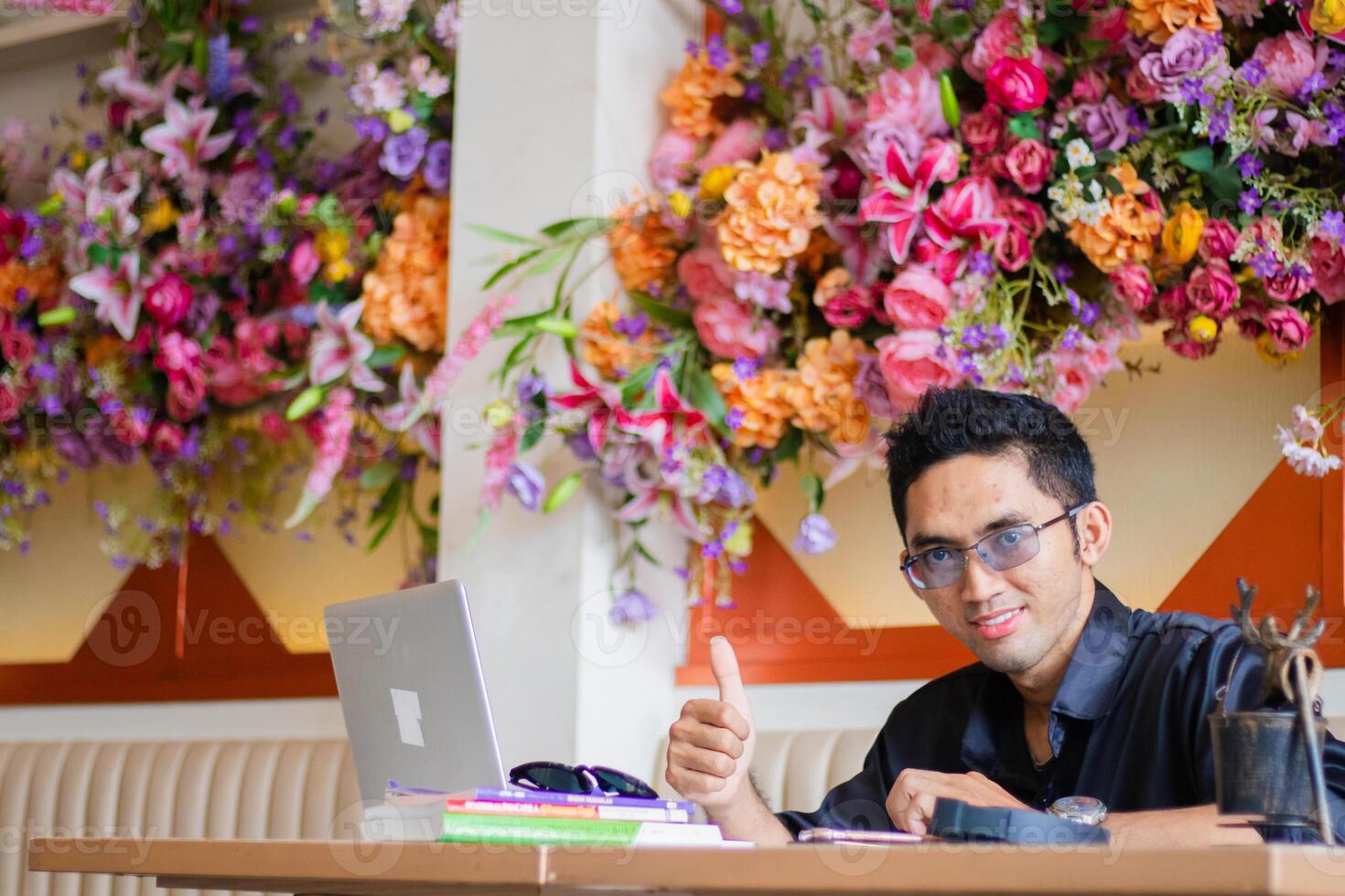Asian male businessman to camera using laptop computer to work on project assignment from client hand thumbs up okay sign at office desk, sitting at workplace cafe photo
