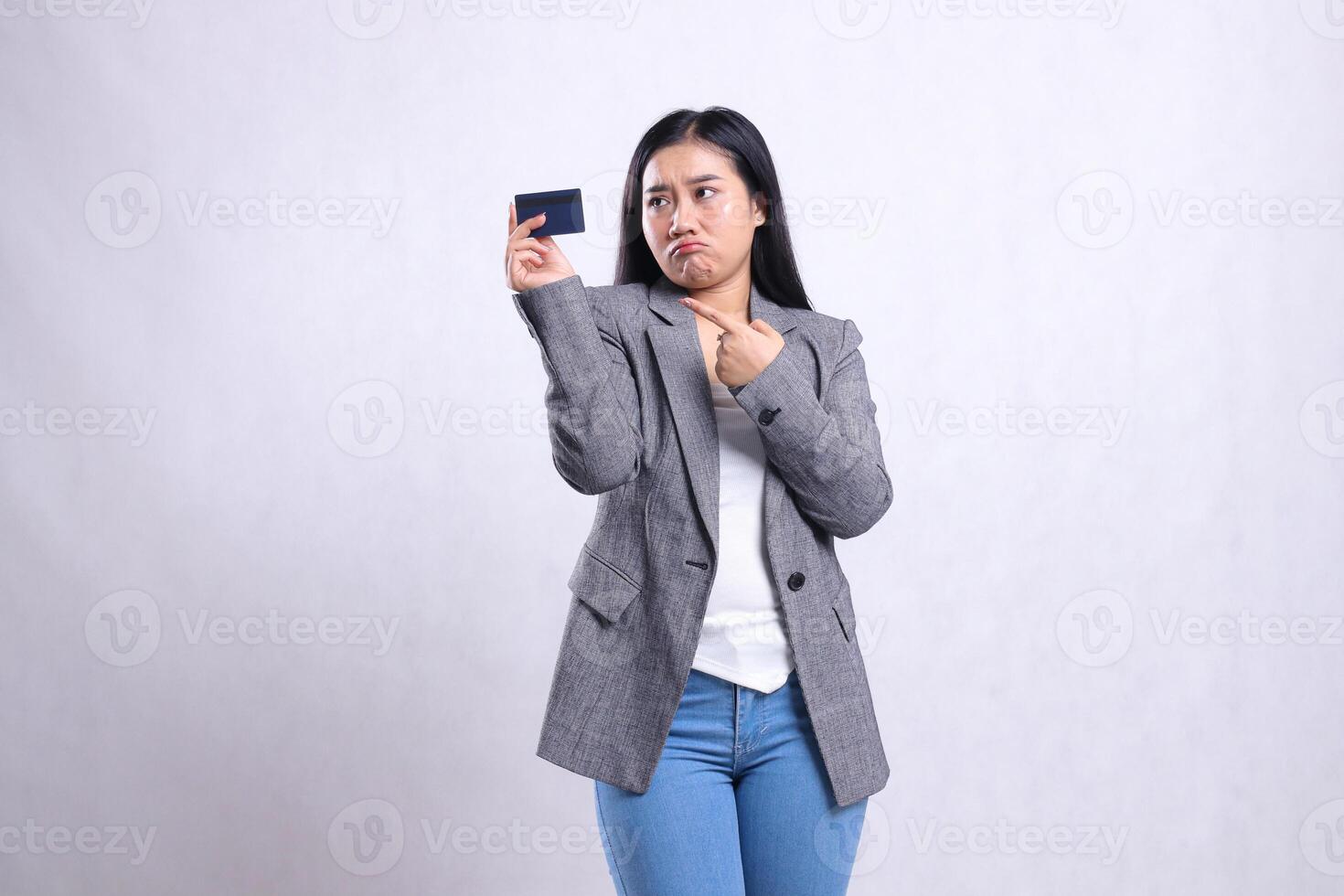 beautiful young office ladies asia pouting looking, pointing and holding debit credit card wearing grey suit standing isolated on white background. for corporate, lifestyle, finance, transaction photo