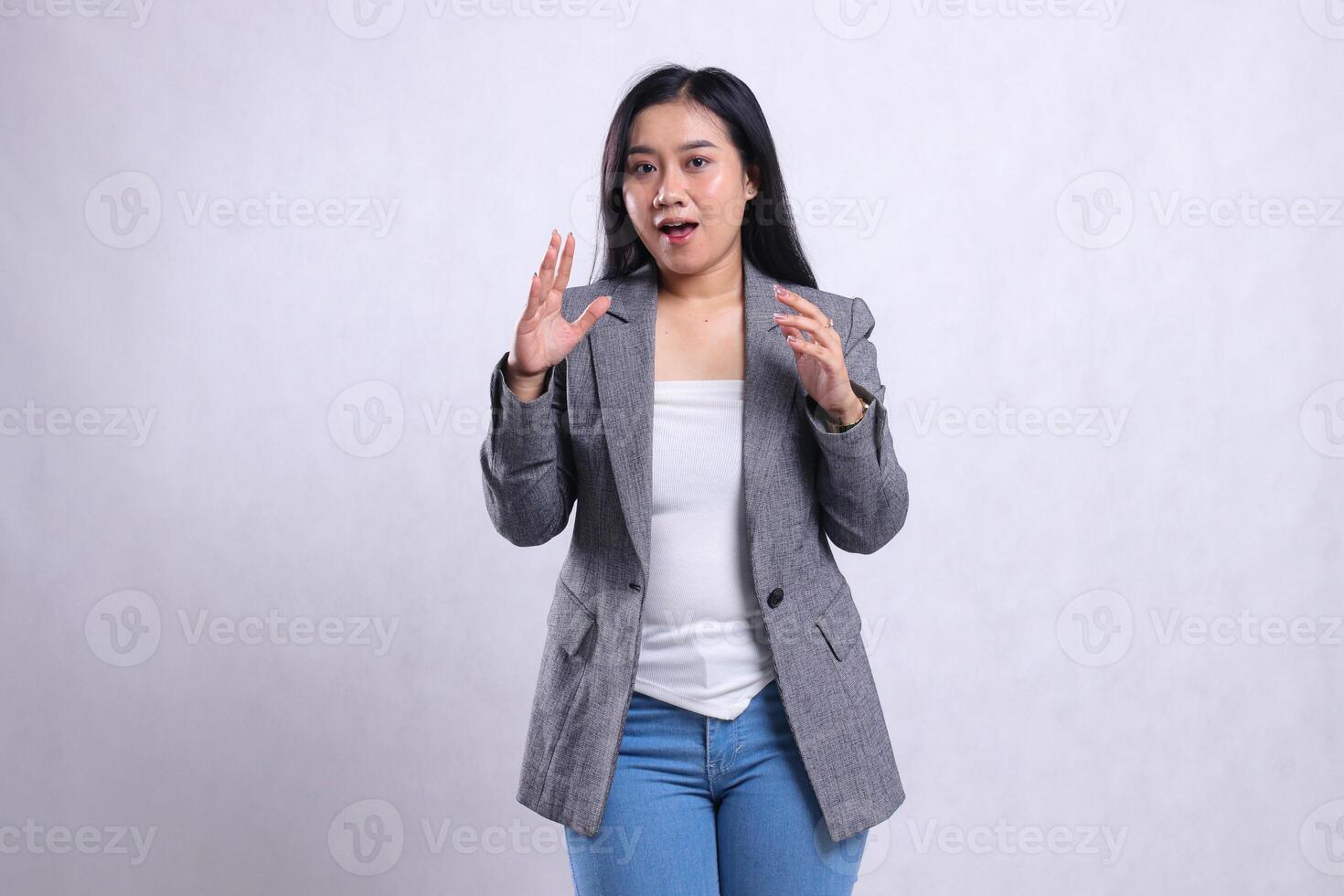 expression of beautiful young woman surprised smiling both arms spread in front of chest wearing grey jacket and jeans standing isolated on white background. for advertising content, fashion, magazine photo