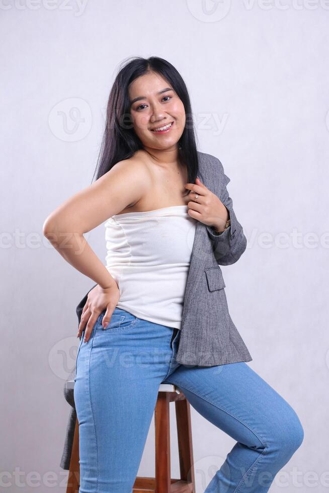 beautiful mature office woman sexy wearing glasses smiling hands on waist and head jacket wearing gray jacket jeans sitting on chair isolated white background. for corporate content, fashion photo