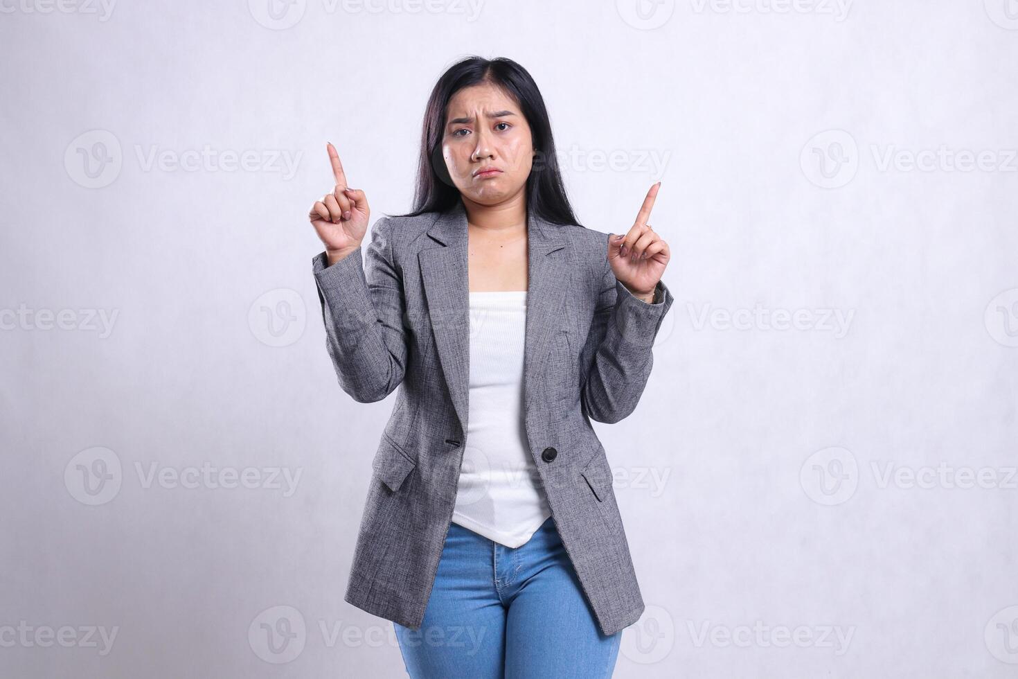 expression of beautiful adult woman asia pouting sad both hands pointing up wearing grey suit and jeans standing isolated on white background. for advertising content, fashion, banner, magazine photo