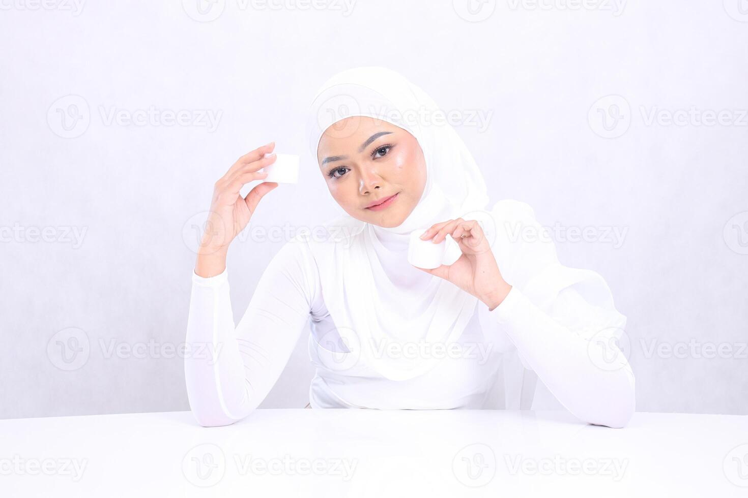 Charm Beautiful young hijab female relax forward both hands holding cosmetic cream satisfied in her skin care routine on white background. Perfect skin, Natural makeup photo