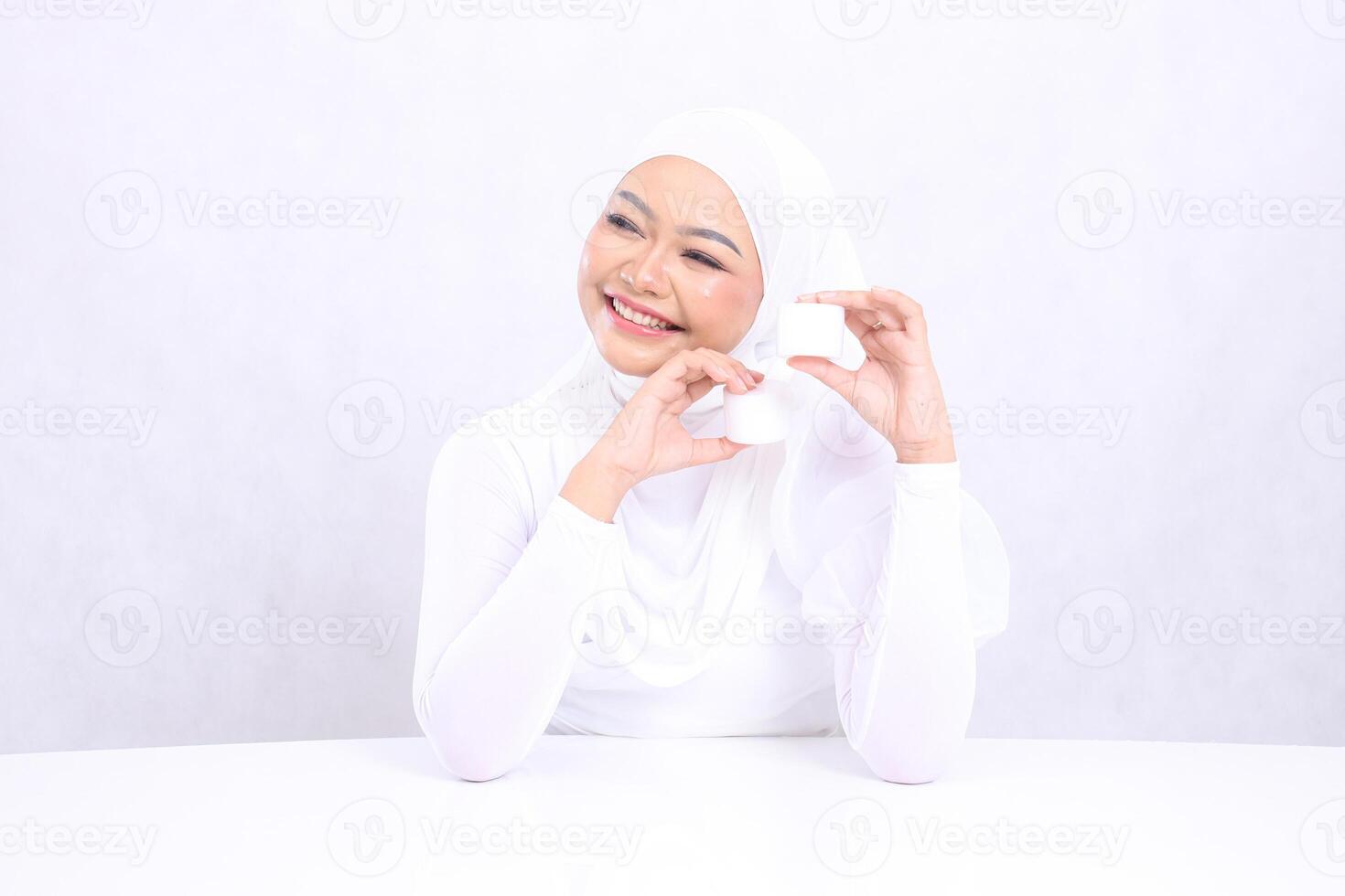 gesture Beautiful young hijab woman happy candid right both hands holding cosmetic cream top bottom for daily skin care routine needs on white background. Facial treatment, Perfect skin photo