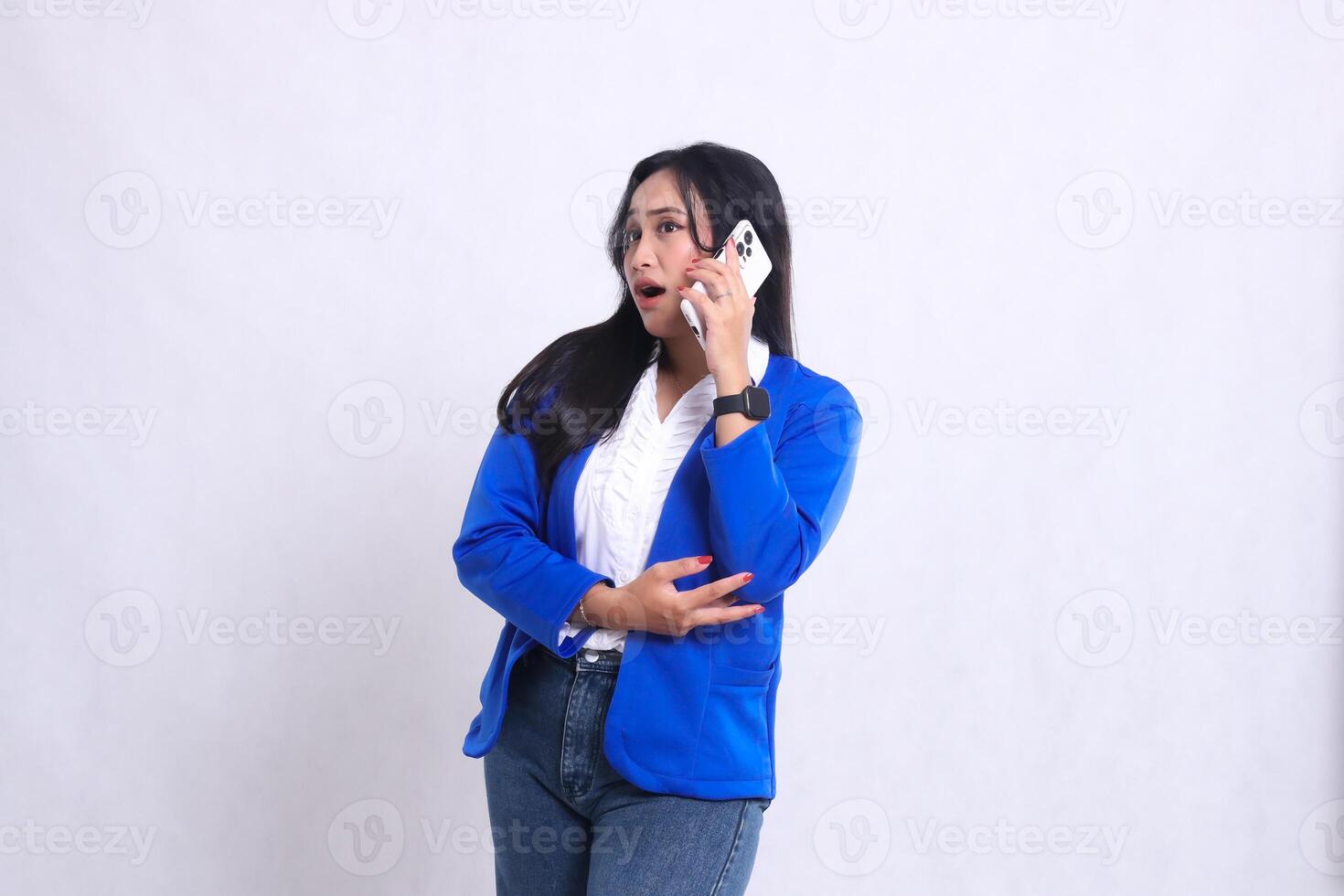 beautiful adult office woman wearing blue formal suit standing shocked candid while talking on the phone using smartphone mobile phone isolated white background. for technology, lifestyle content photo