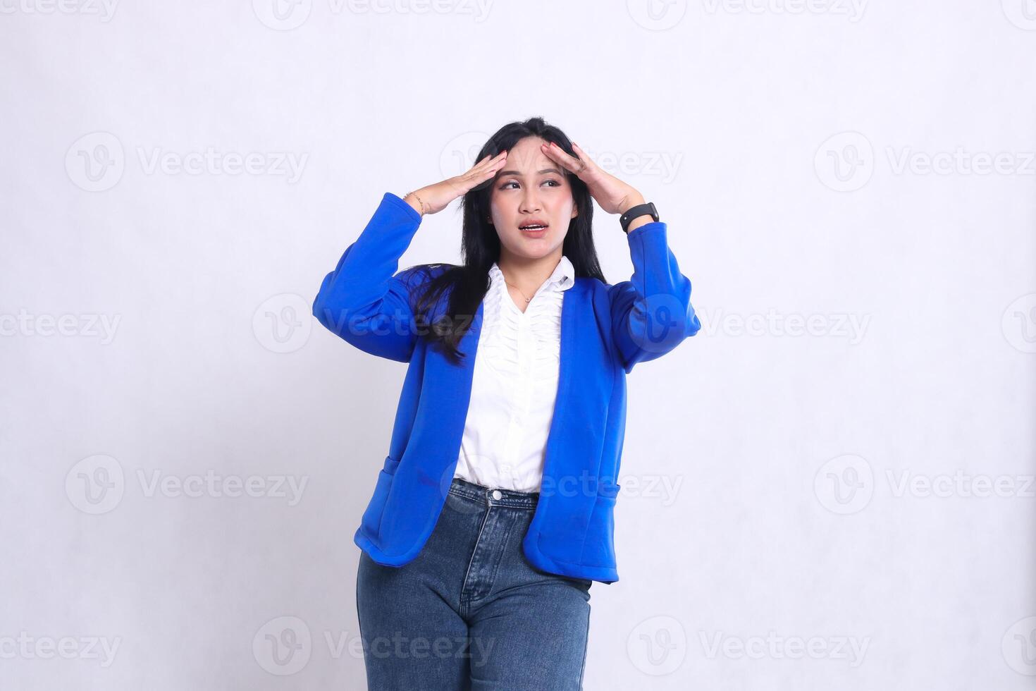 expression of beautiful young office woman wearing blue formal suit standing in front of camera screaming dizzy with both hands holding her head. for company, health, business, care, lifestyle content photo