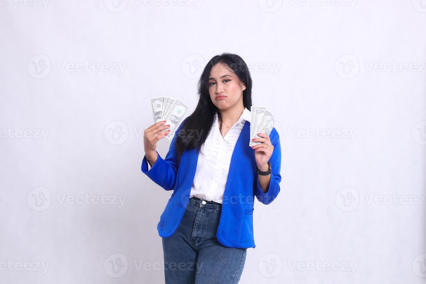 beautiful adult office woman wearing blue formal suit standing pouting to camera holding dollar bills to right and left isolated on white background. for transaction, finance, business content photo